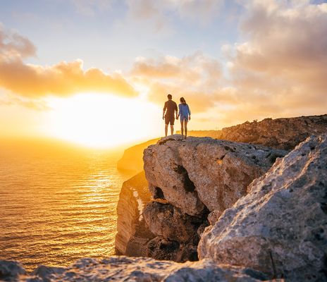 Ein Paar steht auf den Klippen und beobachtet den Sonnenuntergang über Malta