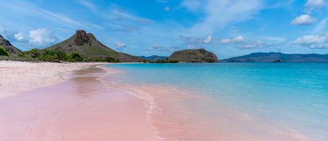 Rosa Sandstrand auf der Insel Komodo mit türkisfarbenem Meer und sanften Hügeln im Hintergrund