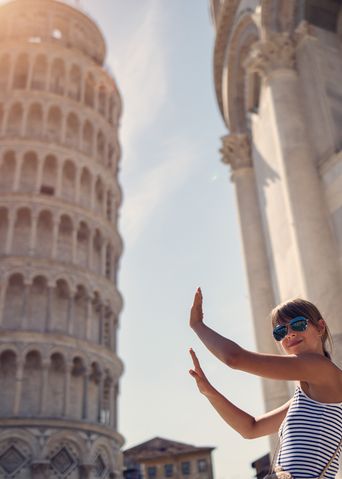 Junges Mädchen steht mit der typischen Handpose vor dem schiefen Turm von Pisa und wird mit einem Handy fotografiert
