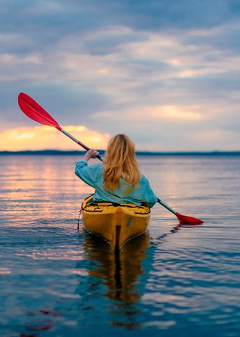 Frau im Kanu von hinten beim Rudern über einen See in Finnland