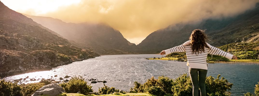 Eine Frau seht auf einem Felsen in Gab of Dunloe in Irland