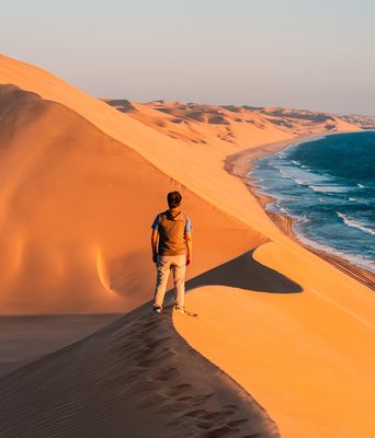 Reisende erklimmen die leuchtend orangefarbenen Dünen bei Walvis Bay in Namibia