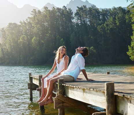 Paar sitzt im Sommer auf einem Steg am See und lacht vor Freude