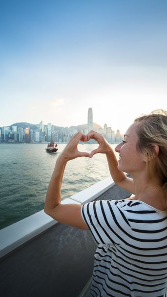 Frau formt Herz mit den Händen vor der Skyline von Hongkong