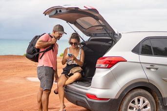 Ein Paar schaut aufs Handy während sie im Kofferraum sitzen und den Weg erkunden