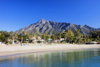 Ruhiger Sandstrand von Marbella mit sanften Wellen und Bergkulisse im Hintergrund