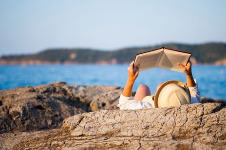 Frau liegt auf einem Felsen und liest ein Buch