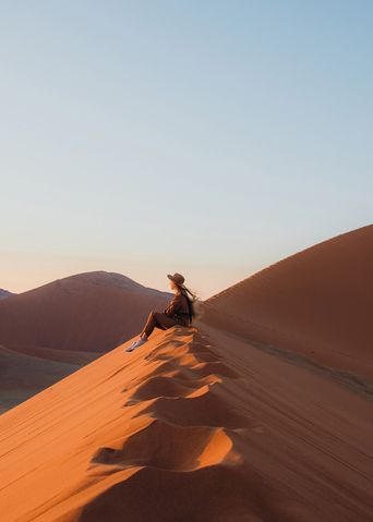 Frau sitzt in der Wüste im Namib Naukluft Nationalpark in Namibia und genießt den Ausblick
