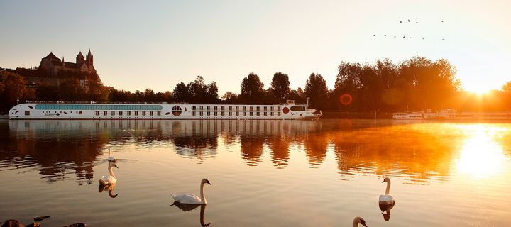A-ROSA Flussschiff Viva vor einem Schloss bei Sonnenuntergang mit Schwänen