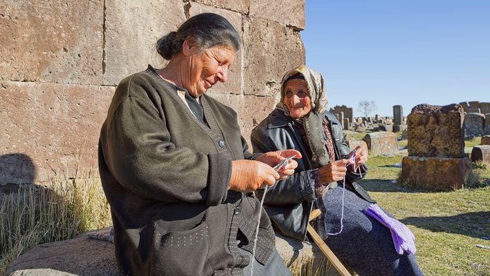 Zwei Frauen sitzen auf einer Mauer und stricken in Armenien
