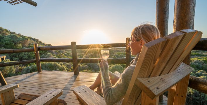 Frau sieht auf einer Terrasse und genießt den Sonnenuntergang mit einem Glas Wein