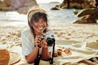 Frau liegt auf einer Decke am Strand mit Kamera und macht Fotos im Sand