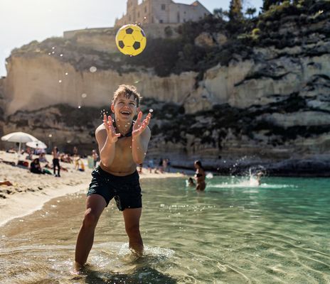 Kind spielt mit einem Ball im klaren türkisfarbenen Meer an einem Sandstrand in Tropea in Kalabrien