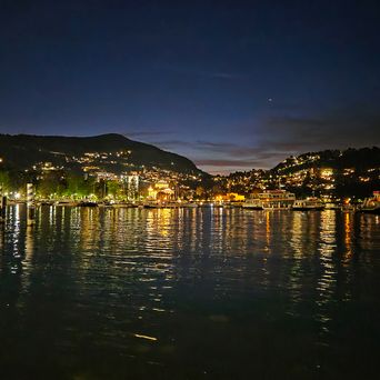 Der Comer See in der Nacht mit glitzernden Lichtern der umliegenden Häuser, Como in Italien