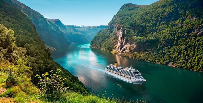 Ein Costa-Kreuzfahrtschiff gleitet durch türkisfarbenes Fjordwasser zwischen bewaldeten Berghängen.