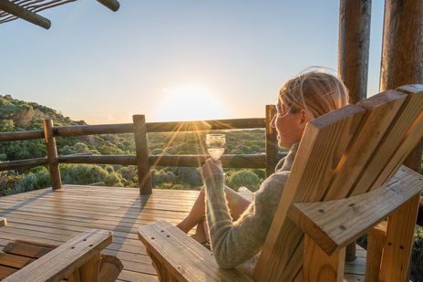Frau sieht auf einer Terrasse und genießt den Sonnenuntergang mit einem Glas Wein