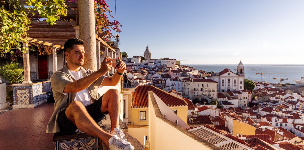 Ein Mann sitzt an einer Balustrade über der Altstadt von Lissabon und genießt die Aussicht