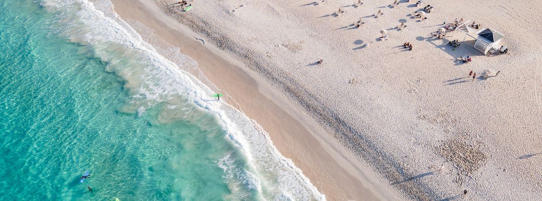 Heller Sandstrand mit sanften Wellen und Surfern auf Fuerteventura, Kanarische Inseln