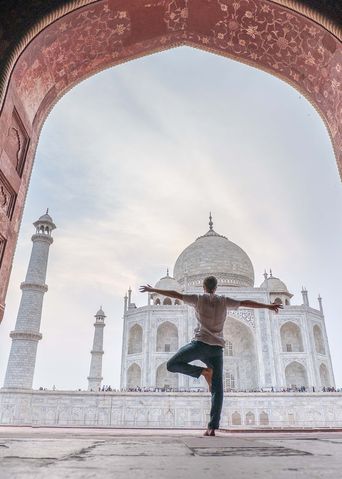 Mann beim Yoga mit Blick durch einen historischen Torbogen auf das Taj Mahal in Agra, Indien