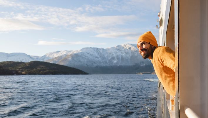 Ein lächelnder Mann lehnt sich aus einem Schiff und bewundert die wunderschöne verschneite Berglandschaft