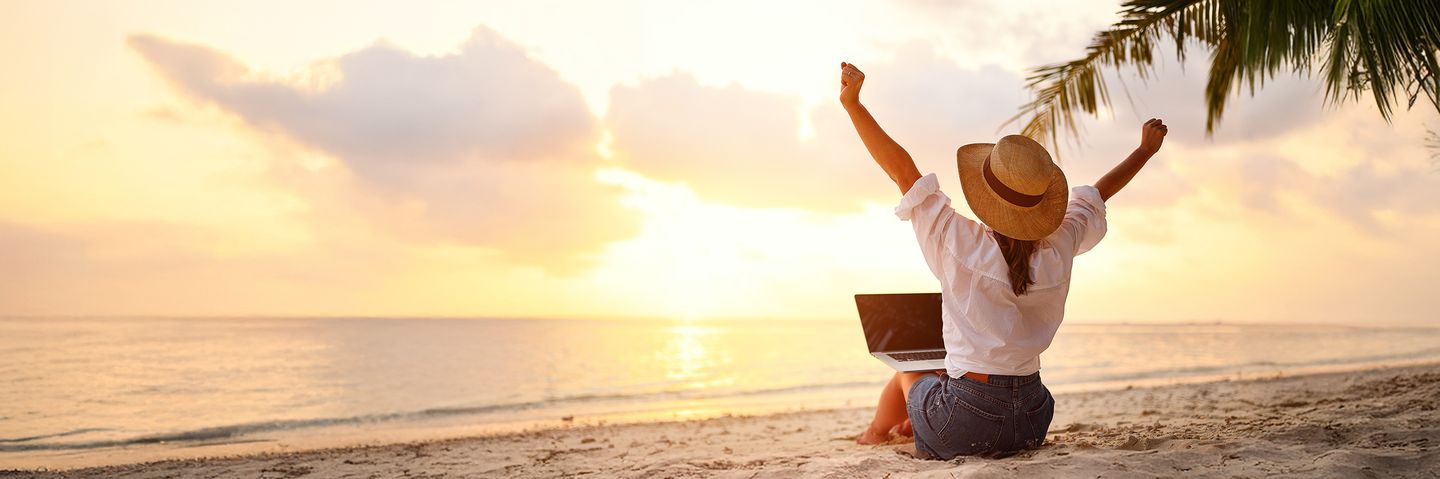 Frau sitzt mit Laptop am Strand und freut sich