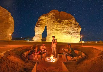 Wüstenlager bei Nacht mit Feuerstelle und beleuchteten Felsen in Saudi-Arabien
