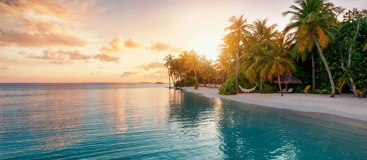 Ruhiger Malediven-Strand bei Sonnenuntergang mit Palmen und spiegelglattem Wasser