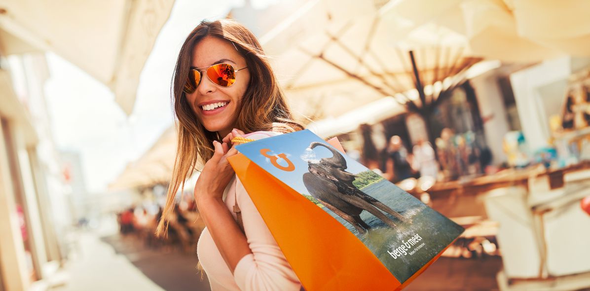 Frau mit Sonnenbrille trägt Einkaufstüte von Berge & Meer beim Bummeln im Einkaufszentrum