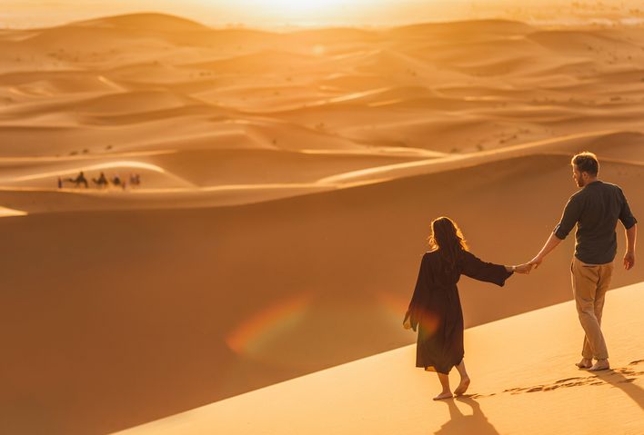Paar geht über eine sandige Dünenlandschaft der Sahara, beleuchtet vom warmen Sonnenlicht