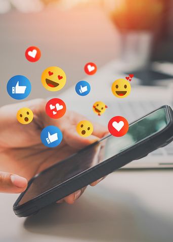 Mann hält Smartphone in der Hand mit Emojis über dem Display 