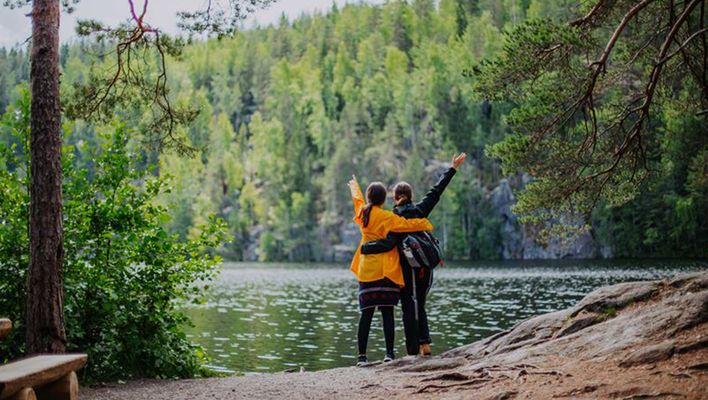 Zwei Reisende stehen am Seeufer in Jyväskylä, Finnland, und blicken auf die bewaldete Landschaft