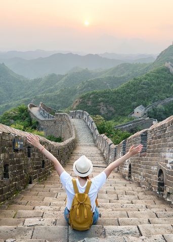 Frau sitzt mit ausgestreckten Armen auf der Großen Mauer in China und genießt den Ausblick