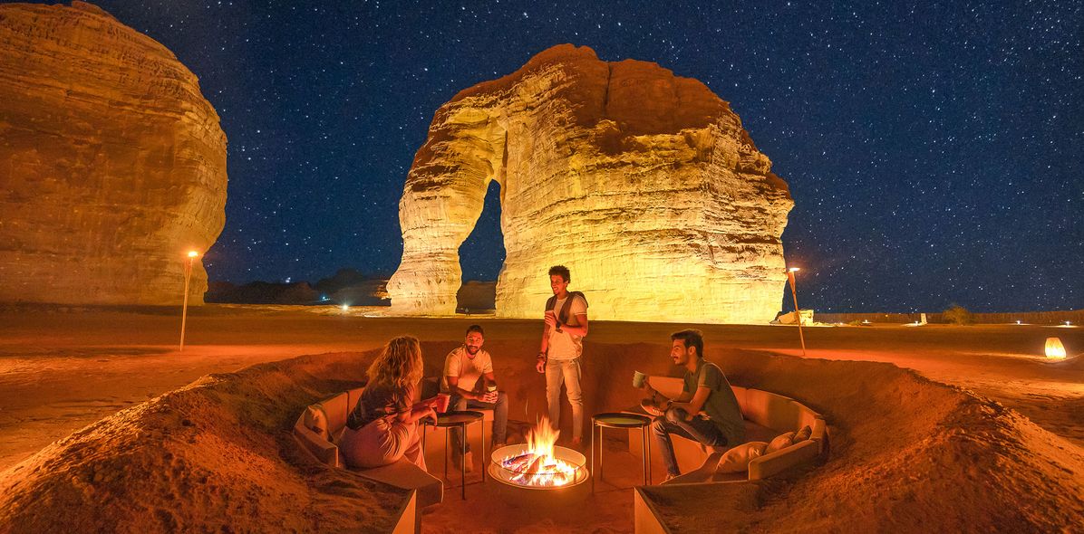 Wüstenlager bei Nacht mit Feuerstelle und beleuchteten Felsen in Saudi-Arabien