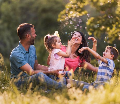 Eine Familie sitzt im Frühling auf einer Wiese und hat Spaß mit Seifenblasen