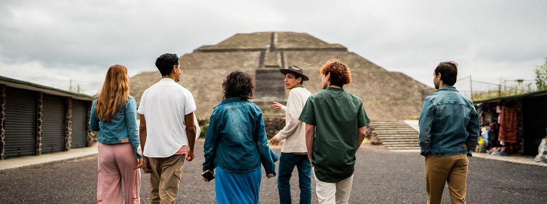 Kleine Reisegruppe geht gemeinsam durch mexikanische Gasse Richtung Pyramide