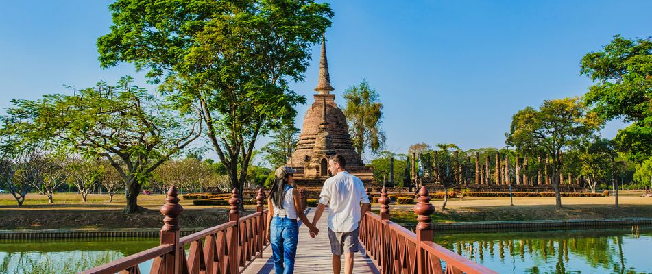 Paar spaziert über eine Brücke in der Tempelanlage von Sukothai