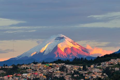 Vulkan Cotopaxi mit schneebedecktem Gipfel über der Stadt im warmen Abendlicht