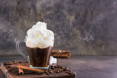 Ein Wiener Kaffee mit Schlagsahne steht neben Zimtstangen und Schokolade auf einem Holztisch