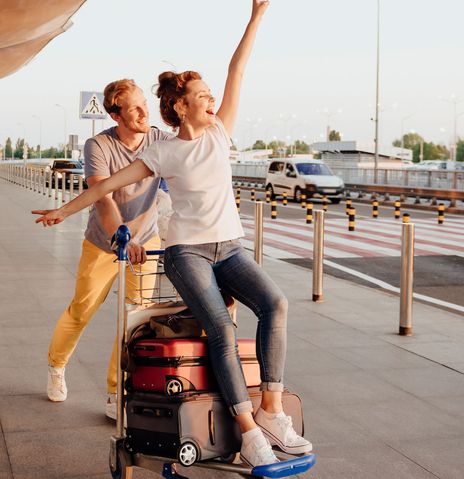 Paar am Flughafen Frau sitzt auf Gepäckwagen