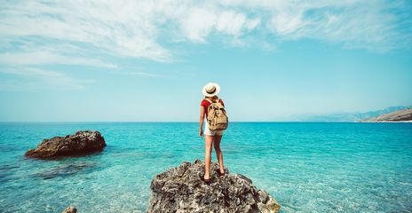 Frau steht auf einem Felsen und schaut auf das Meer