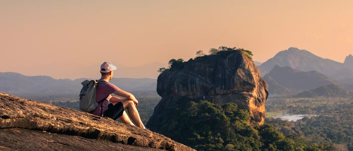 Reisender sitzt auf einem Felsen mit Blick auf den berühmten Löwenfelsen Sigiriya im Zentrum Sri Lankas