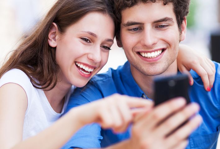 Frau und Mann gucken Arm in Arm interessiert in ein Handy und lachen