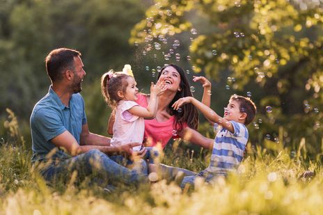 Eine Familie sitzt im Frühling auf einer Wiese und hat Spaß mit Seifenblasen