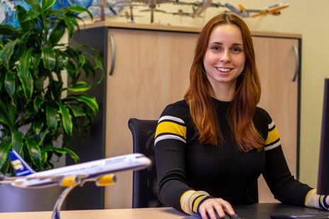 Kollegin Alicia sitzt an ihrem Arbeitsplatz und strahlt in die Kamera