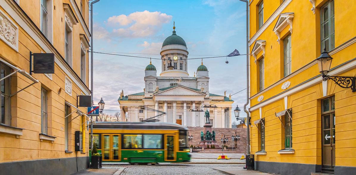 Blick durch eine Gasse auf die Kathedrale von Helsinki mit einer vorbeifahrenden Straßenbahn im Vordergrund, Finnland