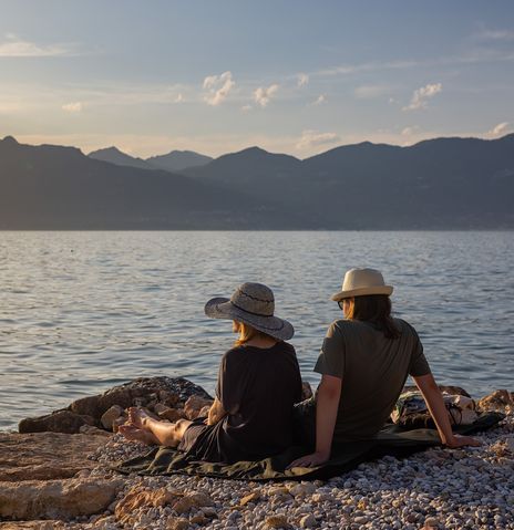 Paar sitzt am Ufer des Gardasees und genießt den Sonnenuntergang mit Blick auf die Berge