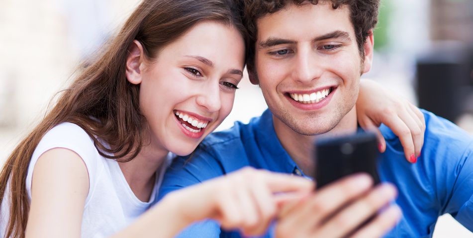 Frau und Mann gucken Arm in Arm interessiert in ein Handy und lachen