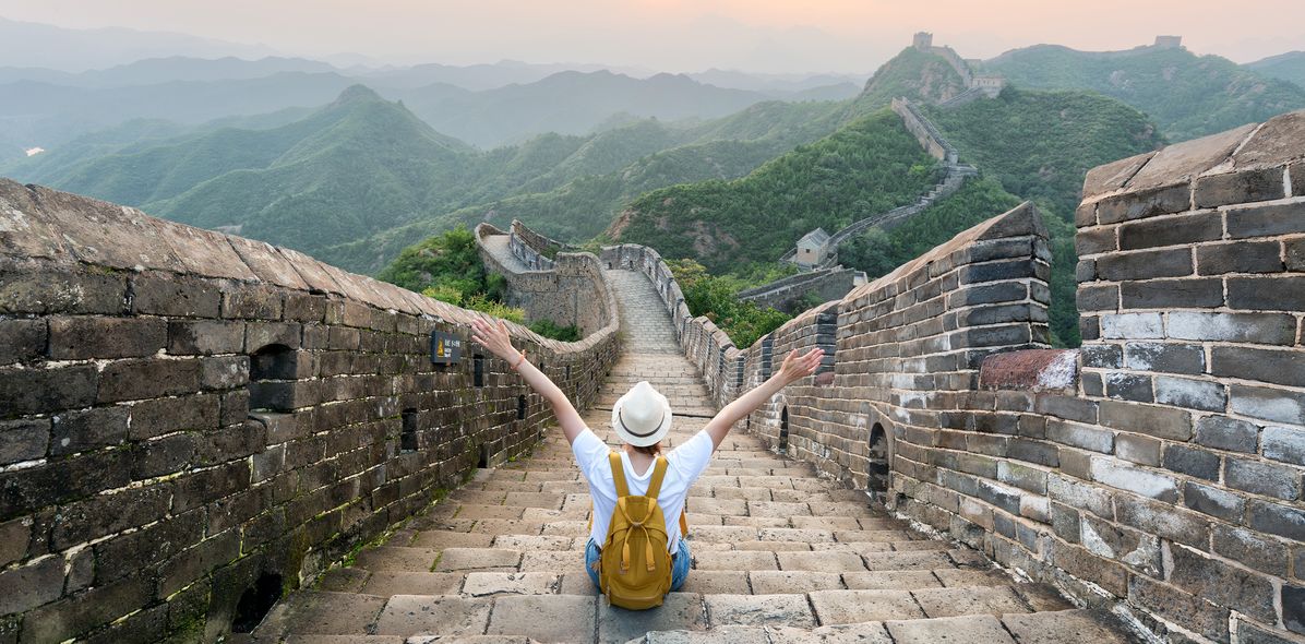 Frau sitzt mit ausgestreckten Armen auf der Großen Mauer in China und genießt den Ausblick