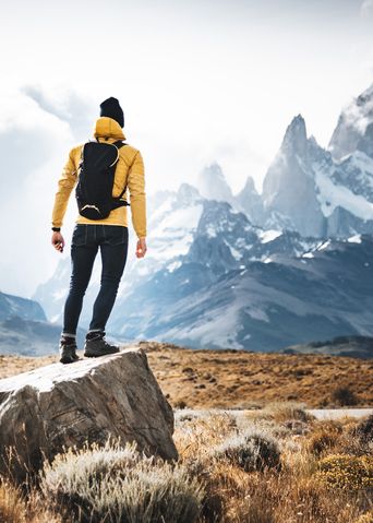 Mann mit Rucksack in Rückansicht steht auf einem Felsstück und blickt auf die Berge von El Chaltén im argentinischen Patagonien