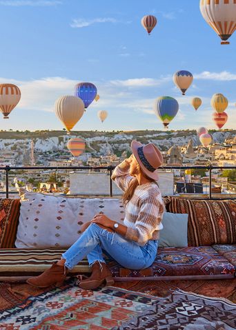 Frau sitzt auf einer Dachterrasse und genießt Ausblick auf die Heißluftballons in Kappadokien